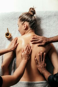 Eine Frau erhält eine Rückenmassage, während mehrere Hände ihren oberen Rücken behandeln.