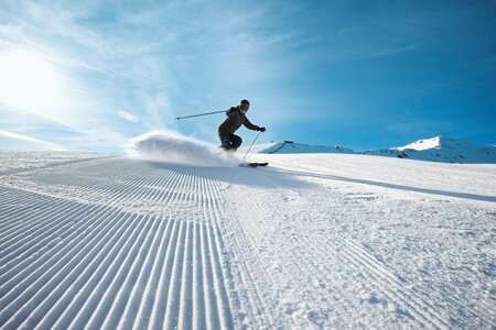 Ein Skifahrer zieht eine Spur über die frisch präparierte Piste unter blauem Himmel.