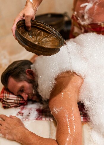 Eine Person liegt bei der Rose-aus-Marrakesch-Behandlung im Kristall Spa, während Wasser über den schaumigen Rücken gegossen wird.