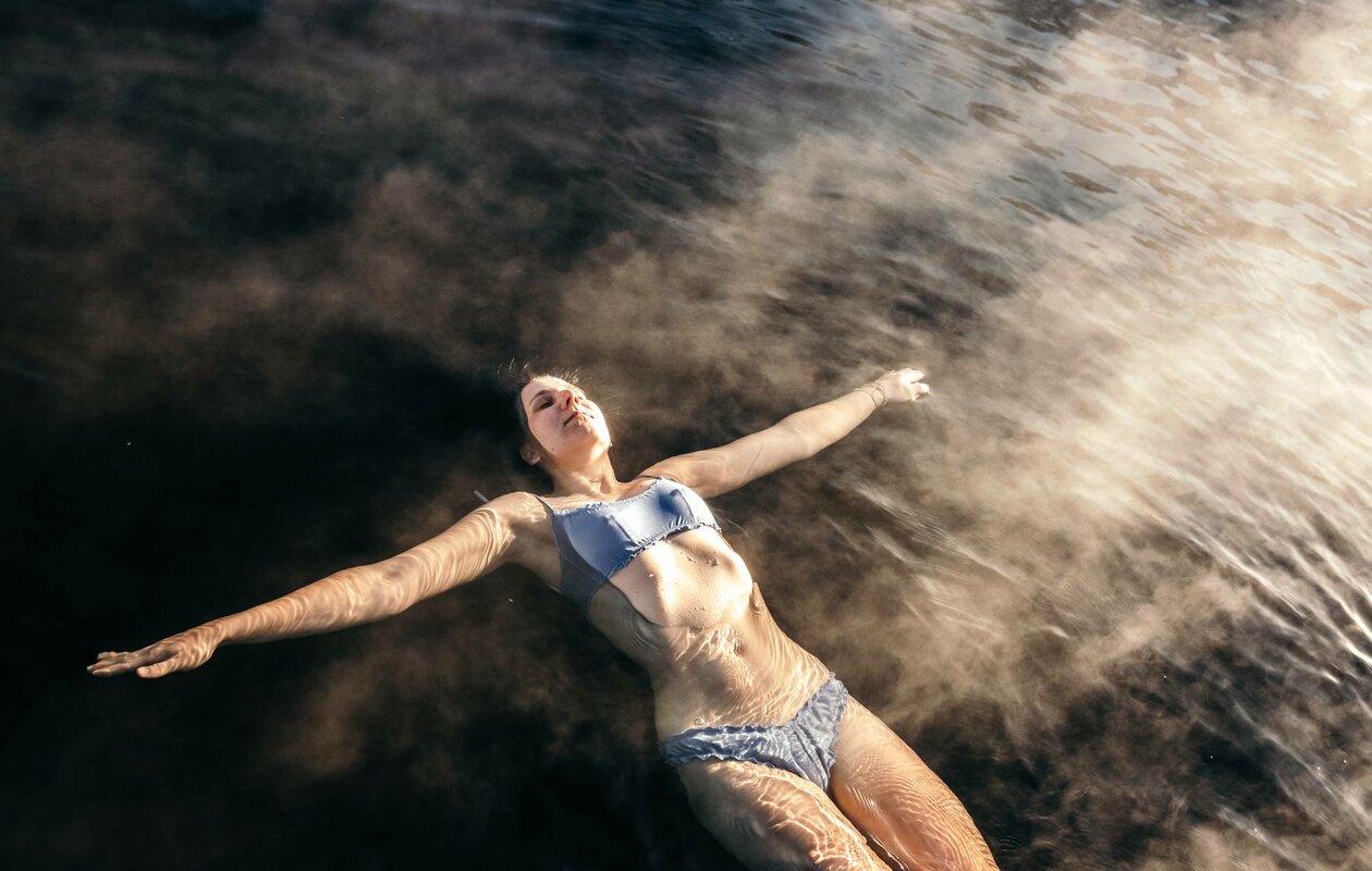 Eine Frau treibt mit ausgebreiteten Armen im Wasser und genießt das See-Bad.