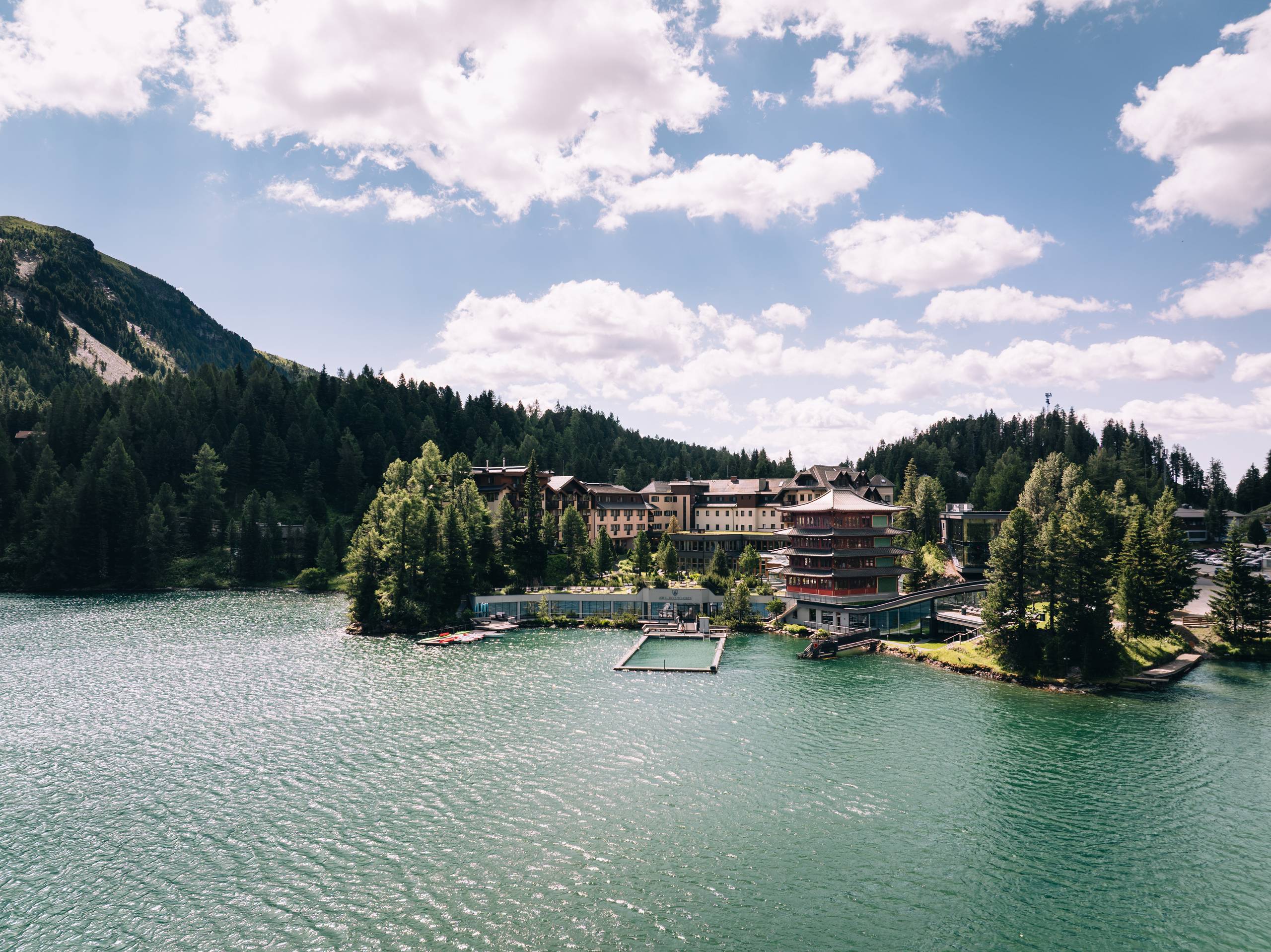 Hotel Hochschober stands on the shore of Lake Turracher See, surrounded by forest and mountains.